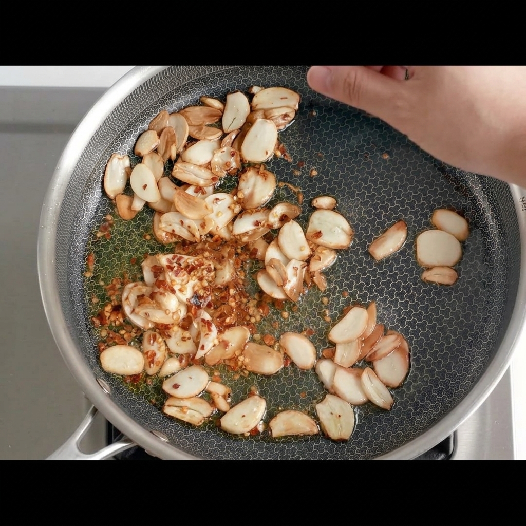 Getrocknete Chilistücke werden zum goldbraunen Knoblauch in die Pfanne gegeben.