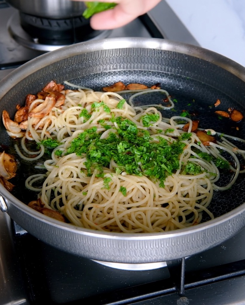 Gehackte frische Petersilie wird über die fertigen Spaghetti in der Pfanne gestreut.