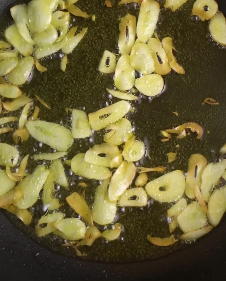 Dünn geschnittener Knoblauch und leuchtend rote Chilischoten braten in schimmerndem Öl in einer Pfanne.