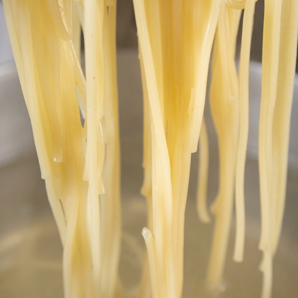 Gekochte Spaghetti-Nudeln werden in eine Pfanne mit goldbraunem Knoblauch und rotem Chili-Öl gegeben.
