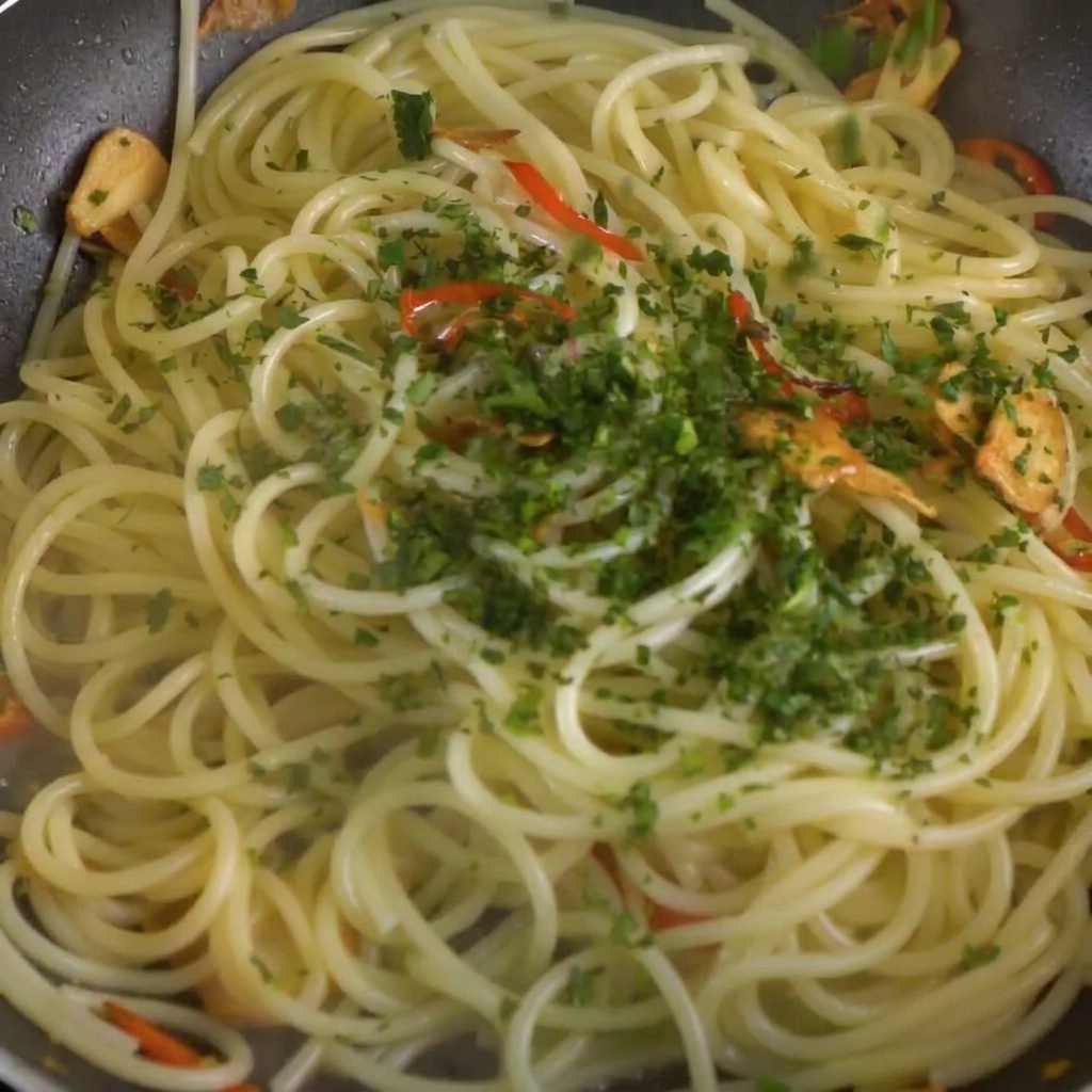 Gehackte frische Petersilie wird über die Spaghetti- und Chili-Knoblauch-Mischung in der Pfanne gestreut.