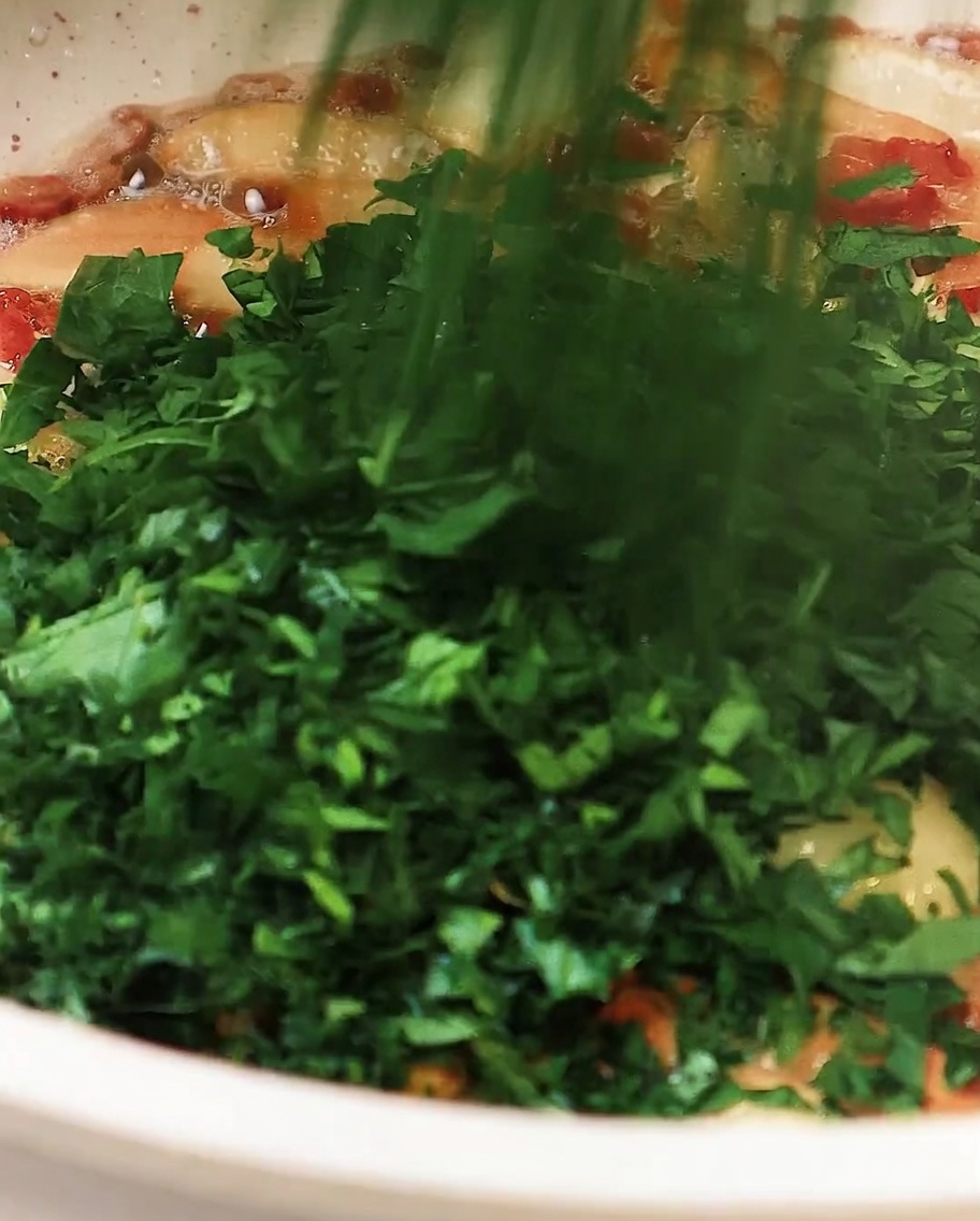 Gehackte Petersilie wird in die Pfanne mit Knoblauch und Speck gegeben und leicht gerührt.