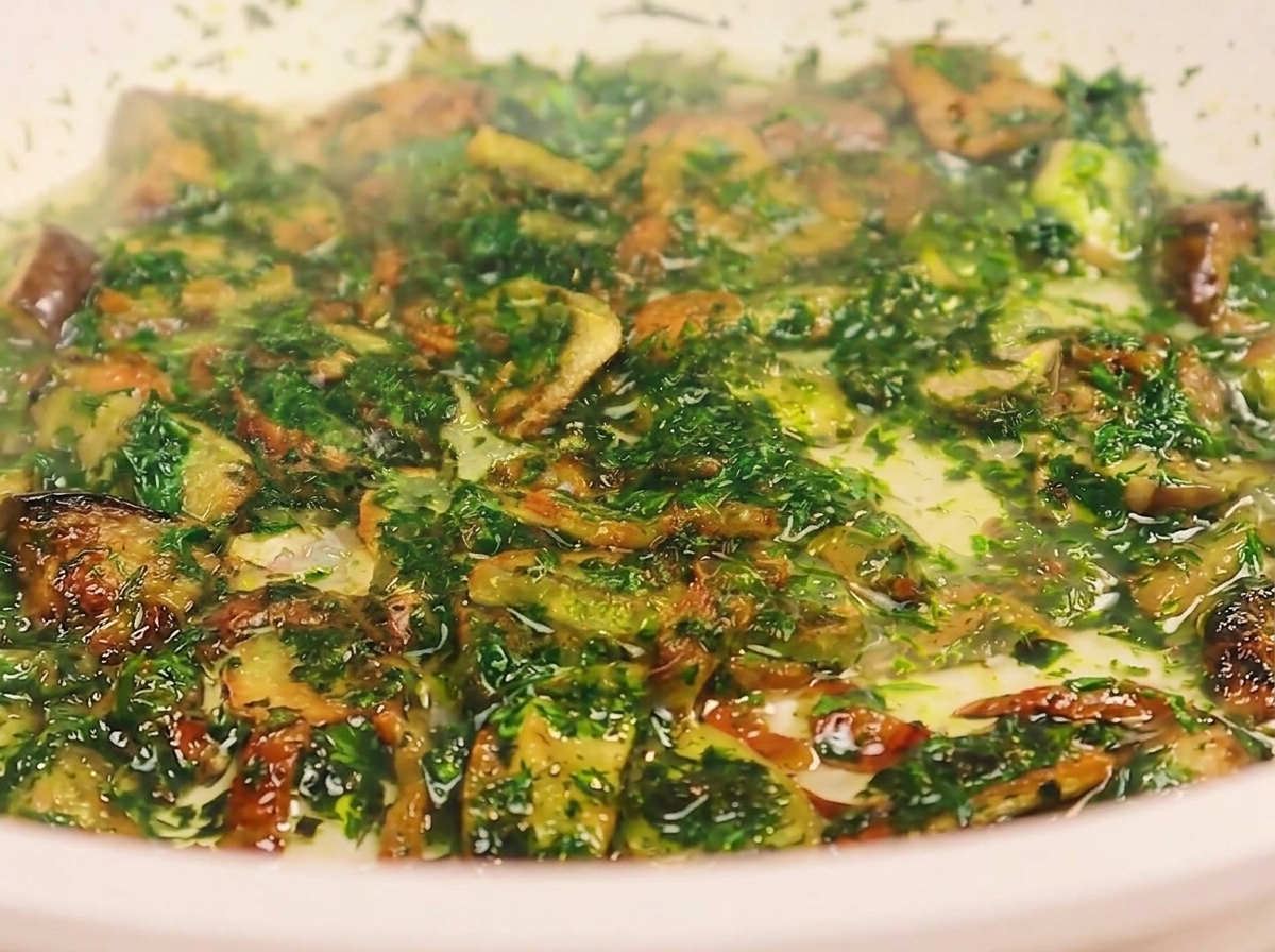 Eine Kelle gießt trübes Nudelwasser in eine Pfanne mit gebratenem Speck, Knoblauch und gehackter Petersilie.