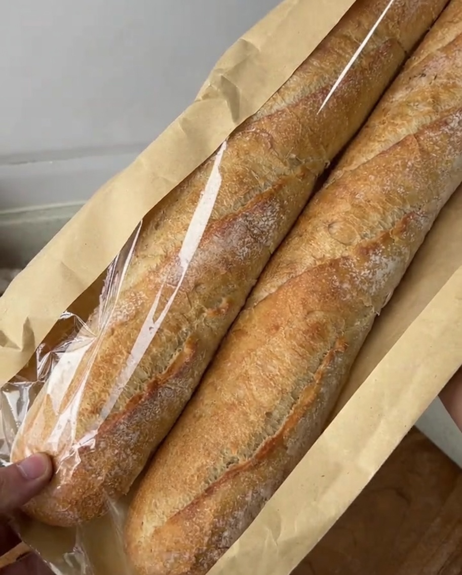 Diagonal aufgeschnittenes Baguette auf einem Holzbrett, bereit für die Knoblauchbutter.