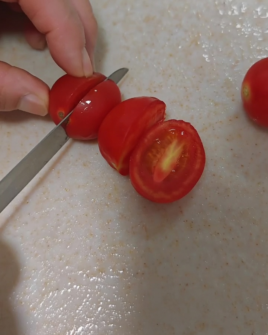 Frische Kirschtomaten werden vorsichtig halbiert.