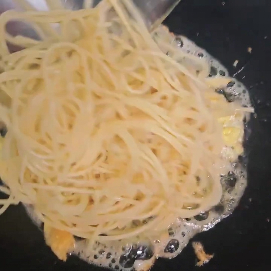 Gekochte Spaghetti werden in den Wok zu den gebratenen Eiern gegeben.