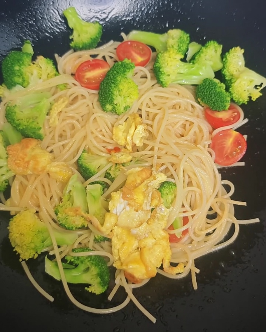 Würzmischung aus einem Päckchen wird über Spaghetti, Brokkoli und Kirschtomaten im Wok gestreut.