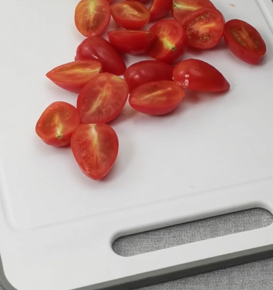 Halbierte Kirschtomaten auf einem weißen Schneidebrett.