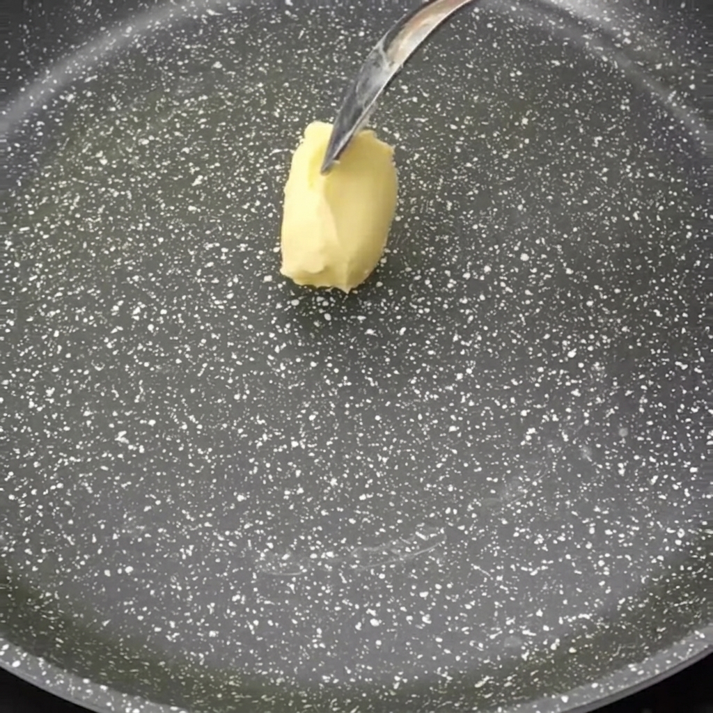 Ein Stück Butter schmilzt in einer dunklen, beschichteten Pfanne.
