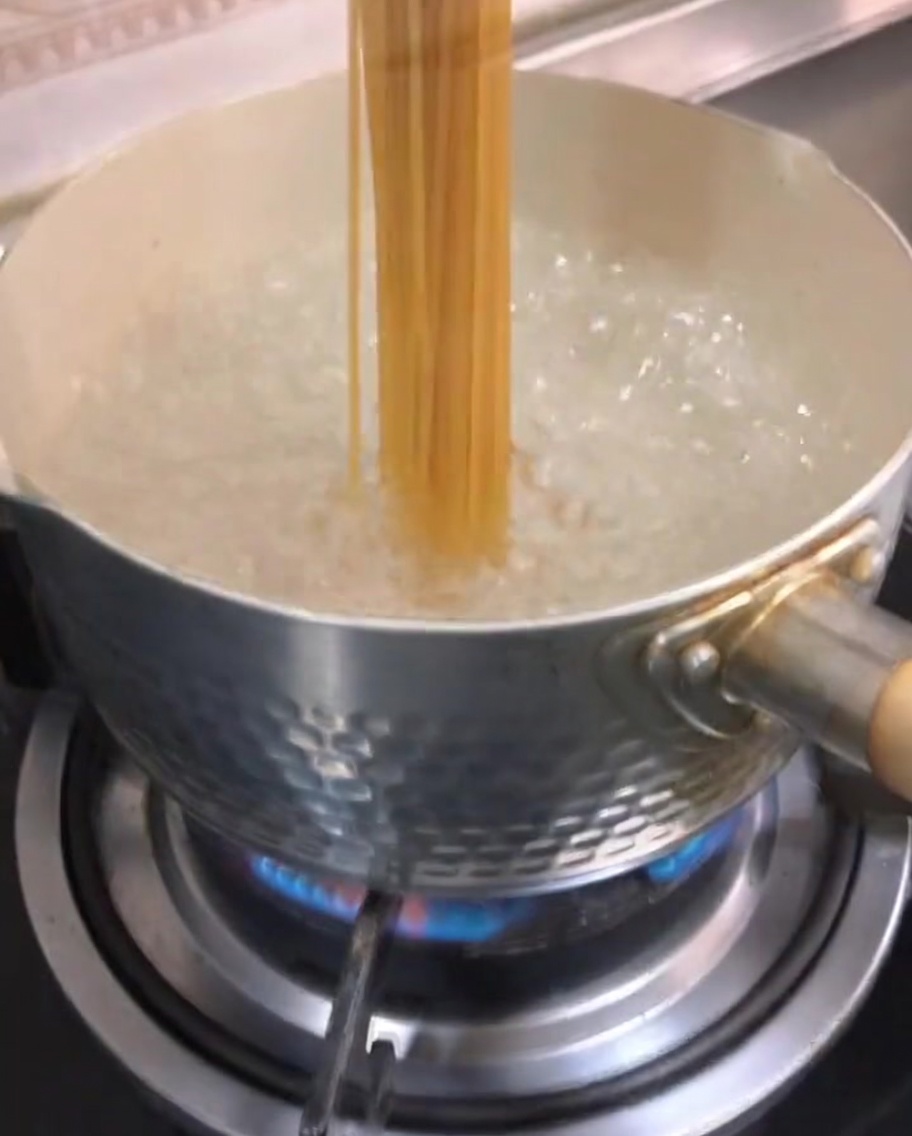 Trockene Spaghetti werden in einen Topf mit kochendem Wasser gegeben.