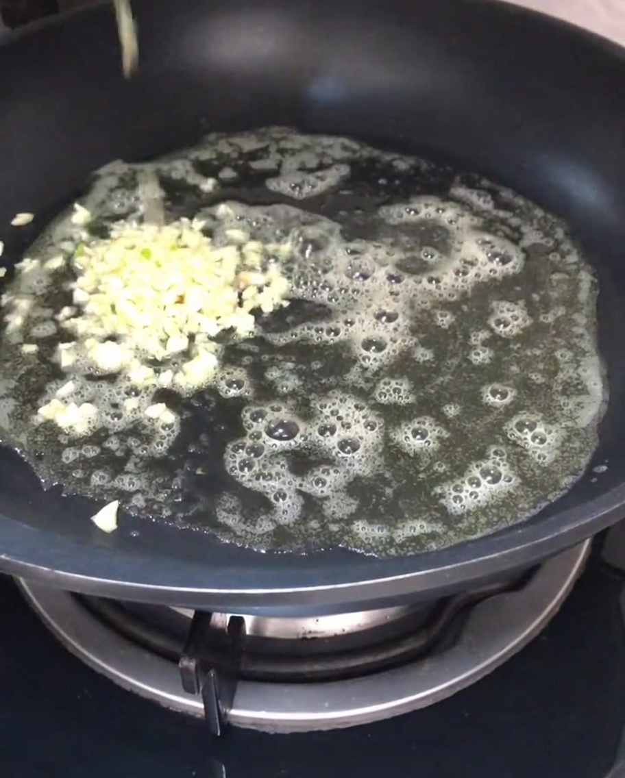 Gehackter Knoblauch brät in geschmolzener Butter in einer Pfanne.