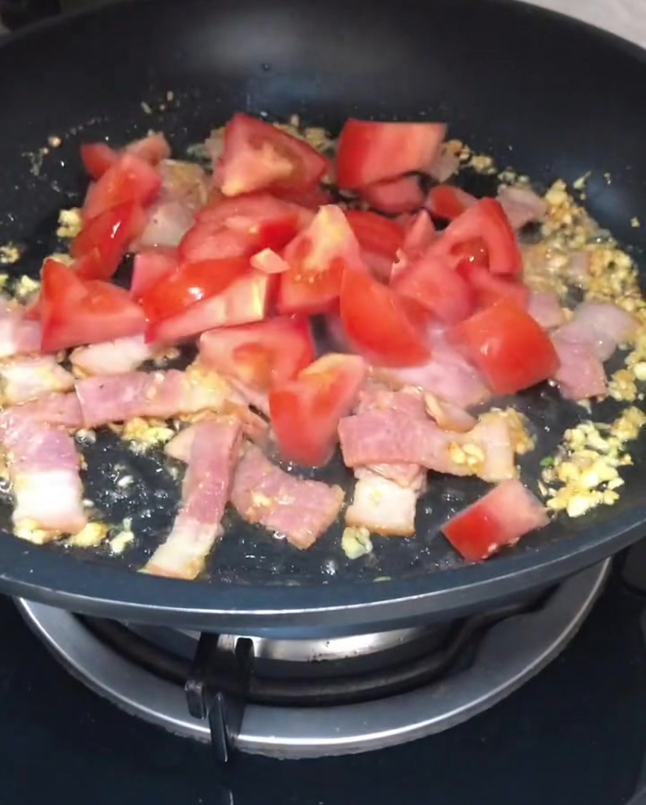 Rote Tomatenstücke werden in die Pfanne zu Speck und Knoblauch gegeben.