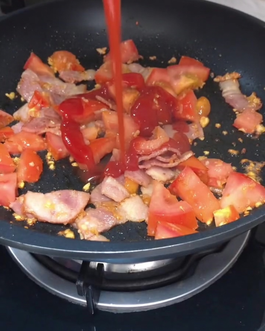 Ketchup und helle Sojasoße werden über die Tomaten-Speck-Mischung gegeben.