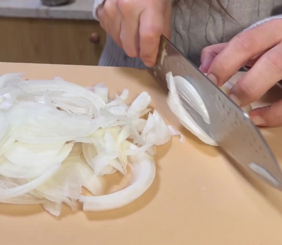 Eine ganze gelbe Zwiebel wird auf einem Schneidebrett in feine Scheiben geschnitten.