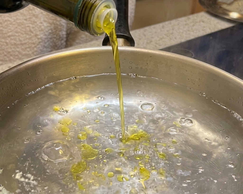 Olivenöl wird in einen Topf mit kochendem Wasser gegossen.
