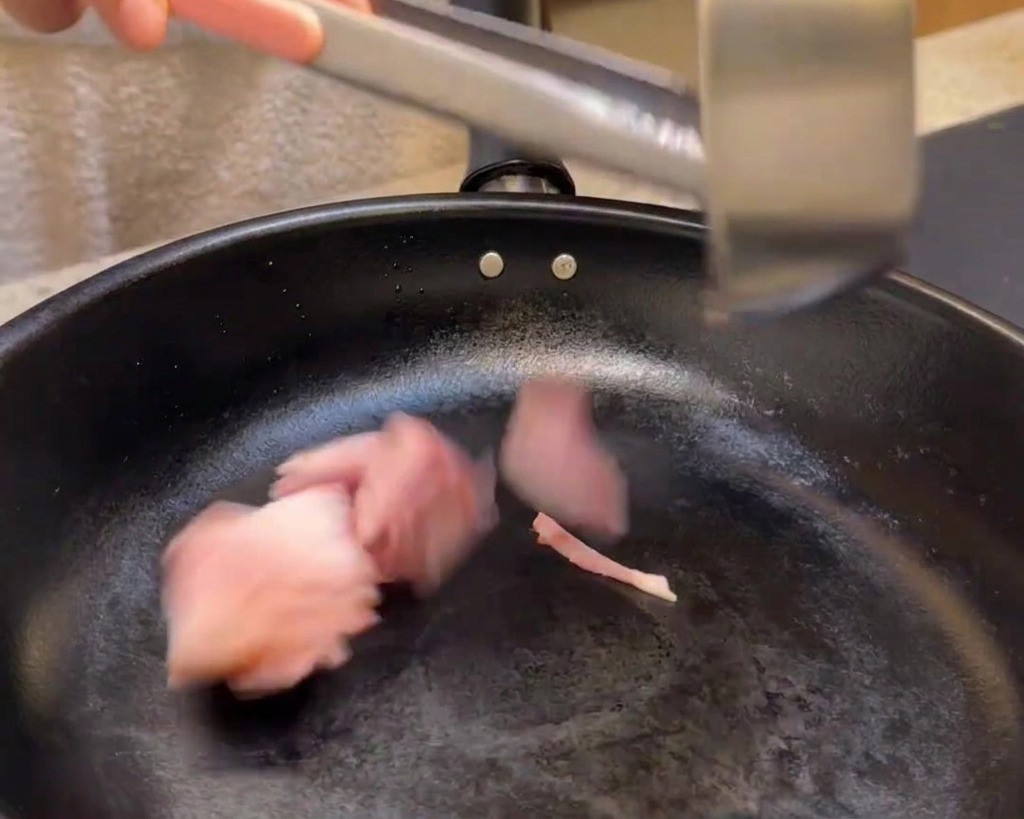 Speckstücke werden zum Braten in eine schwarze Pfanne gegeben.