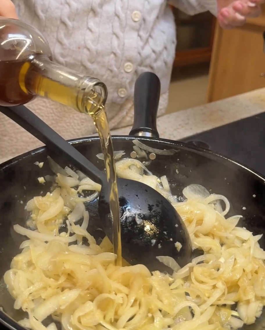 Weißwein und Balsamico-Essig werden in eine Pfanne mit sautierten Zwiebeln und Knoblauch gegossen.
