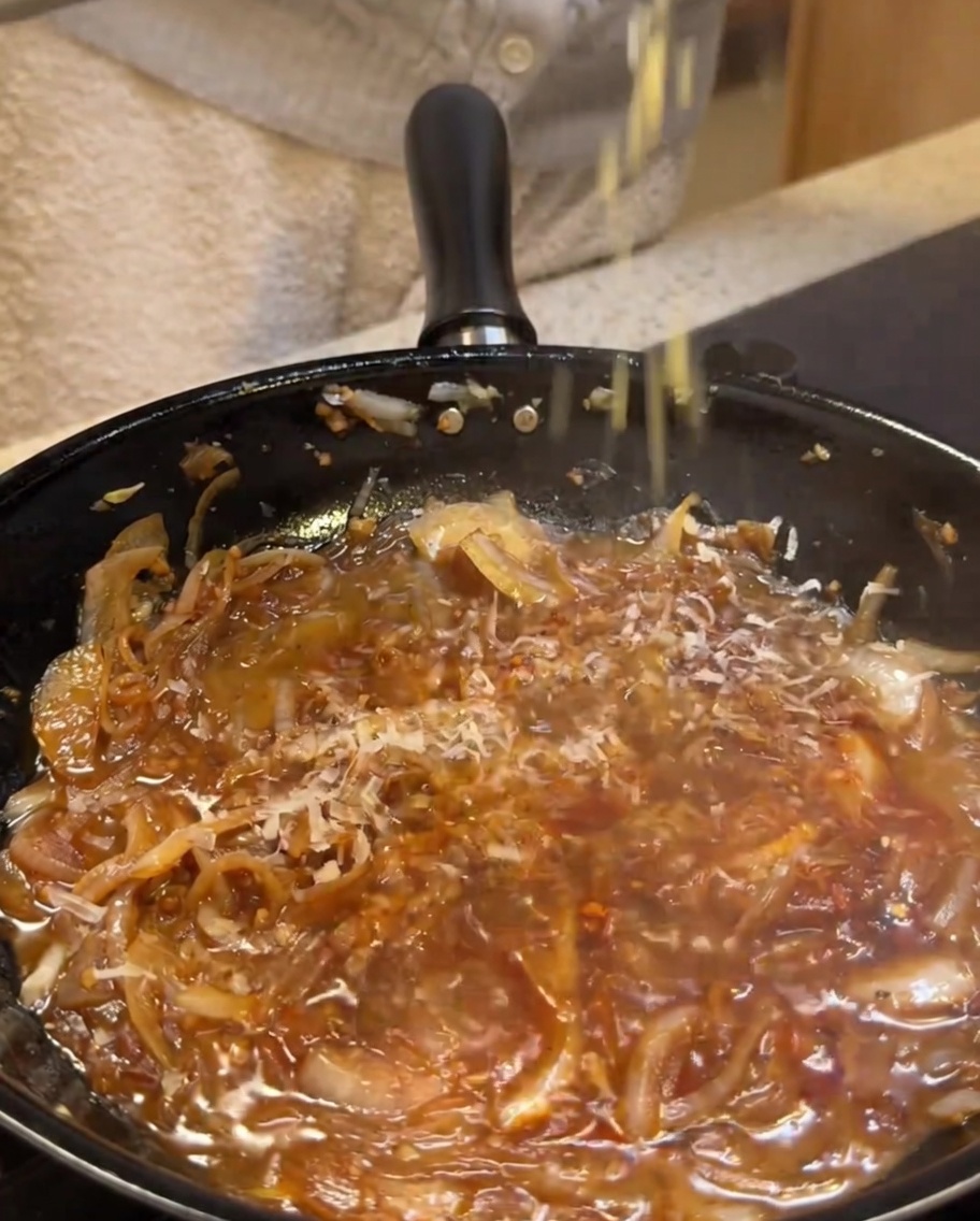 Parmesankäse wird in eine cremige, köchelnde Saucenbasis gerieben.