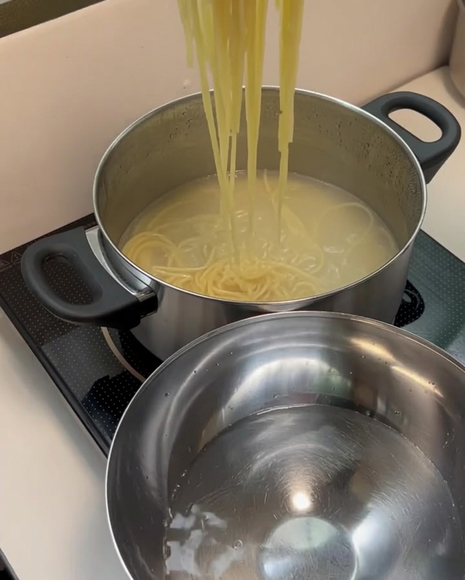Abgetropfte gekochte Spaghetti werden in eine Edelstahlschüssel mit frischem, kaltem Wasser gegeben.