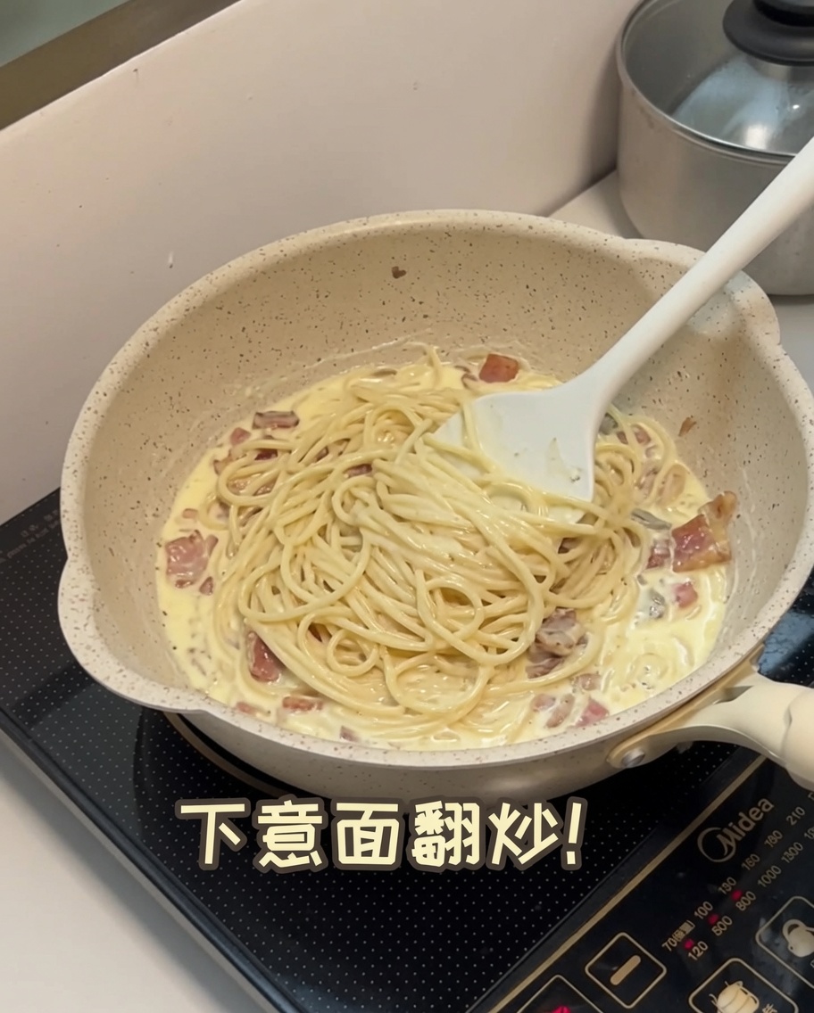 Gekochte Spaghetti werden in die cremige Pilzsauce in der Pfanne geschwenkt.