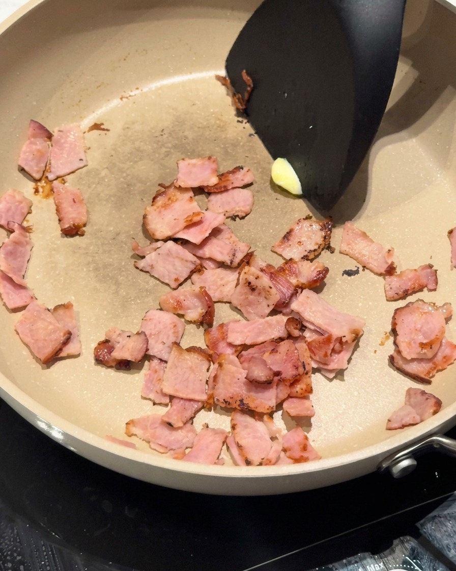Ein Stück gelbe Butter schmilzt in der Pfanne neben den gebräunten Speckstücken.
