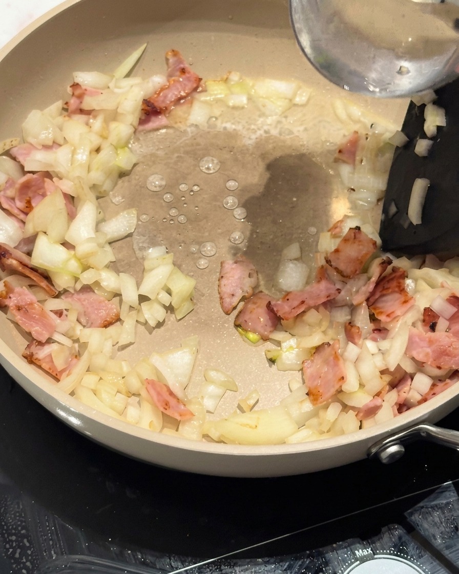 Spiralnudeln werden in die Pfanne auf die Speck-Zwiebel-Basis gelegt.
