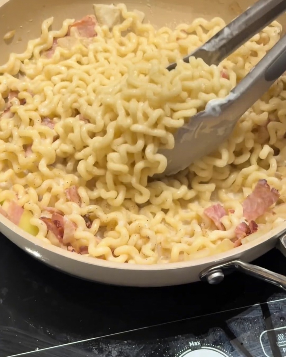 Parmesankäse wird über eine Pfanne mit cremiger Carbonara-Pasta gestreut.