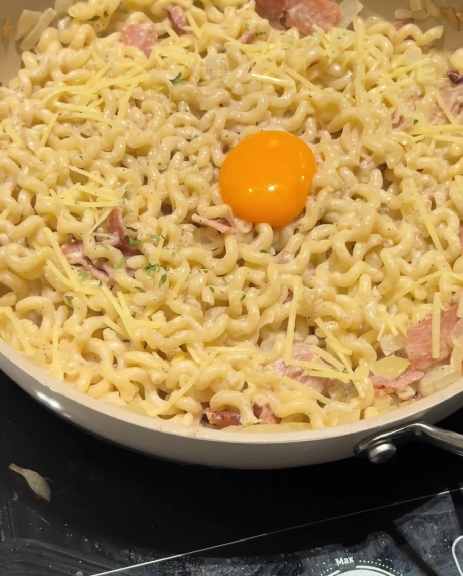 Getrocknete Petersilie wird als finales Garnieren über das Eigelb und die cremige Carbonara gestreut.