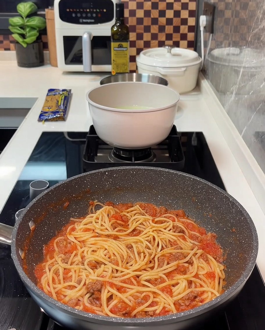 Spaghetti mit Sauce in der Pfanne, belegt mit Käsescheiben.