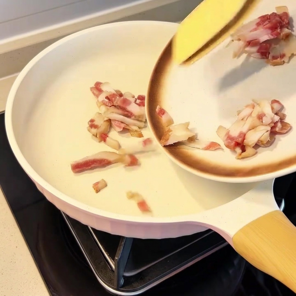 Gleichmäßig in einer kalten Pfanne verteilte Guanciale-Stücke.