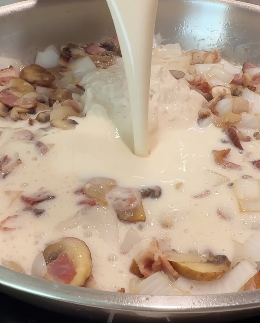 Eine Tasse Milch wird in die Pfanne gegossen, um sie mit der Alfredo-Soße und den angebratenen Zutaten zu vermischen.