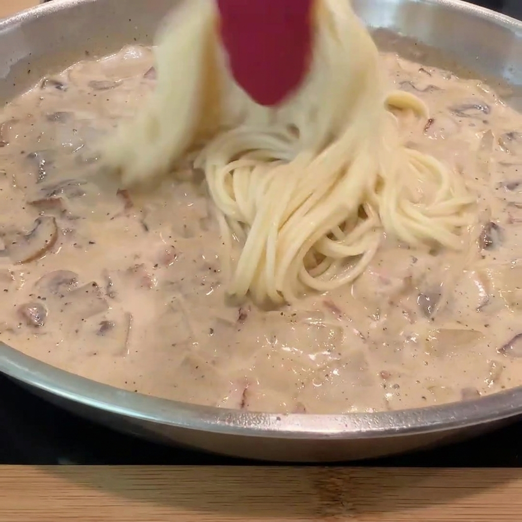 Gekochte Spaghetti werden in die Pfanne mit der cremigen Soße und den restlichen Zutaten gegeben.