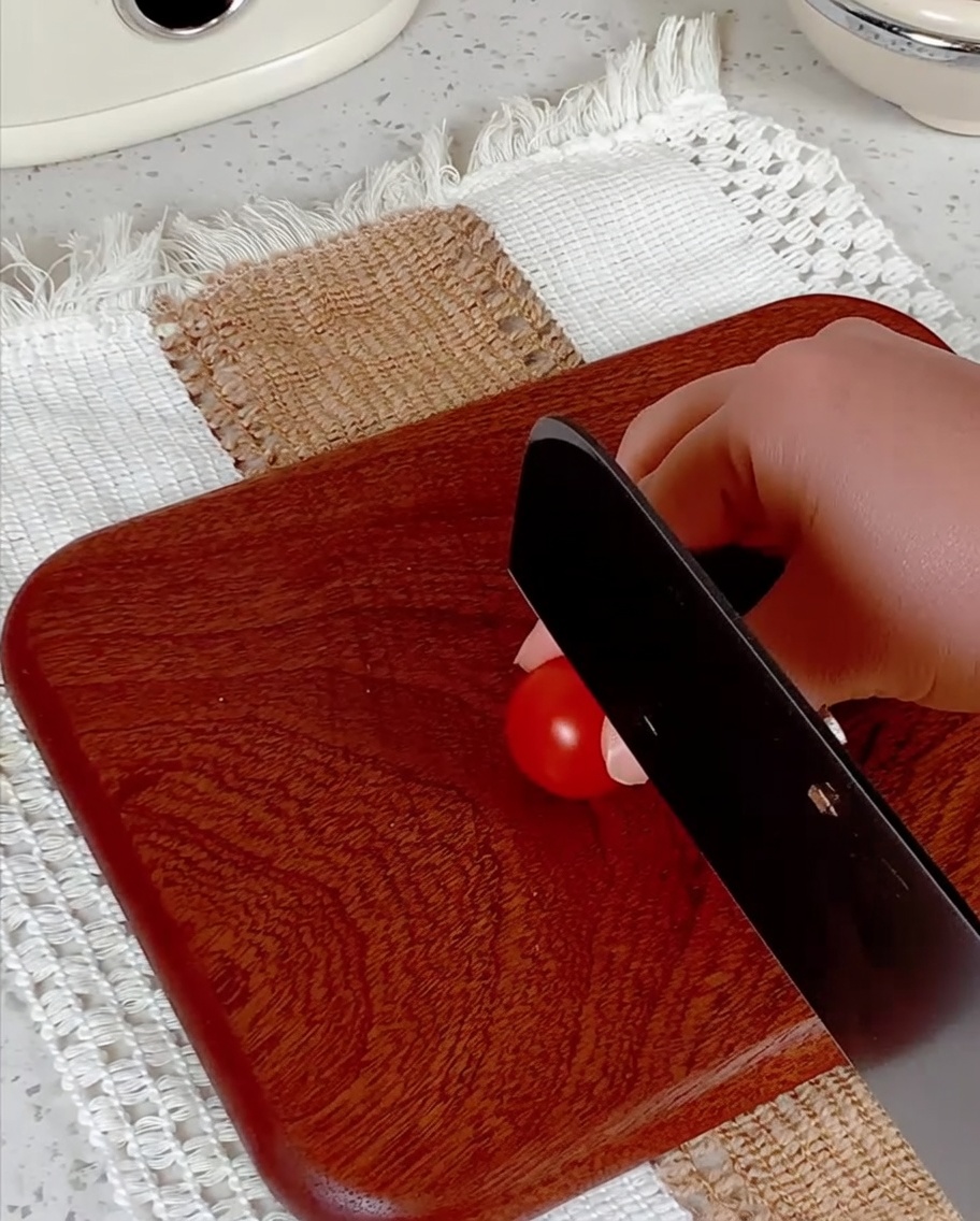 Kirschtomaten werden auf einem Holzbrett mit einem Messer halbiert.