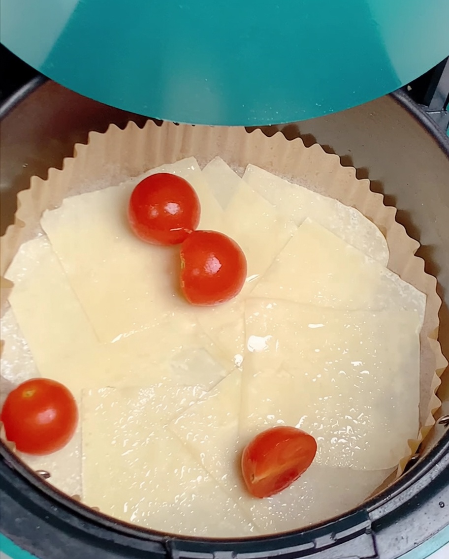 Kirschtomatenhälften sind über den geölten Teigblättern im Air-Fryer-Korb verteilt.
