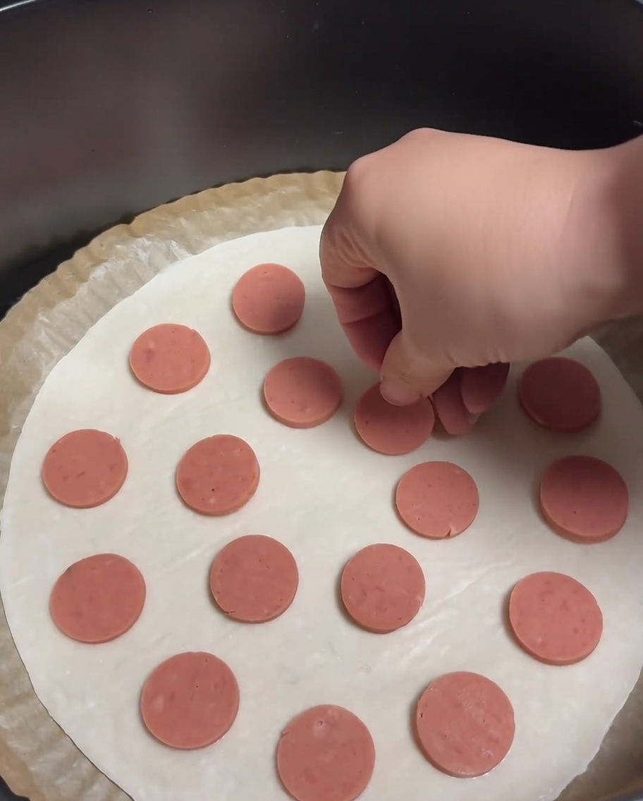 Ein Frühlingszwiebel-Pfannkuchen, belegt mit gleichmäßig verteilten runden Wurstscheiben.