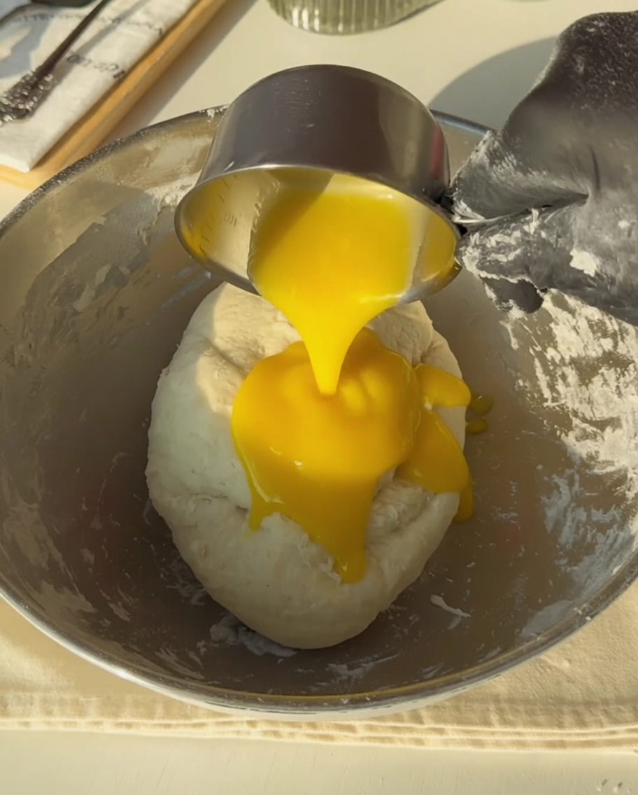 Behandschuhte Hand gießt goldene geschmolzene Butter auf den Teig.