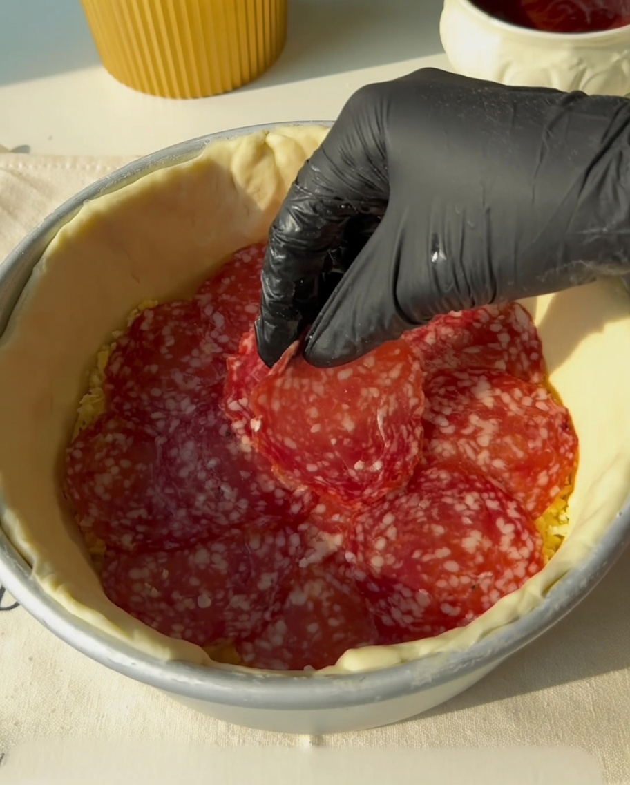 Speckstreifen werden auf die Salamischicht gelegt.