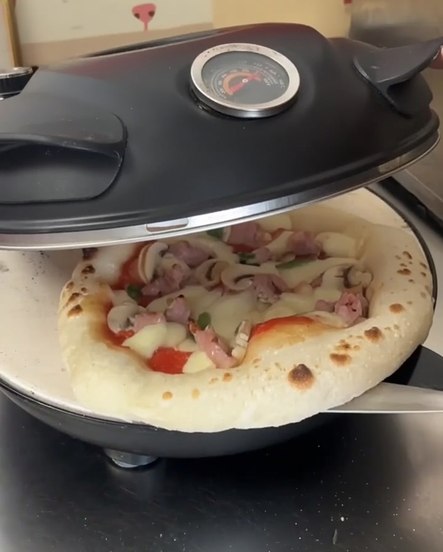 Eine halb gebackene Pizza wird in einem offenen Pizzaofen mit einem Metallschieber gedreht.
