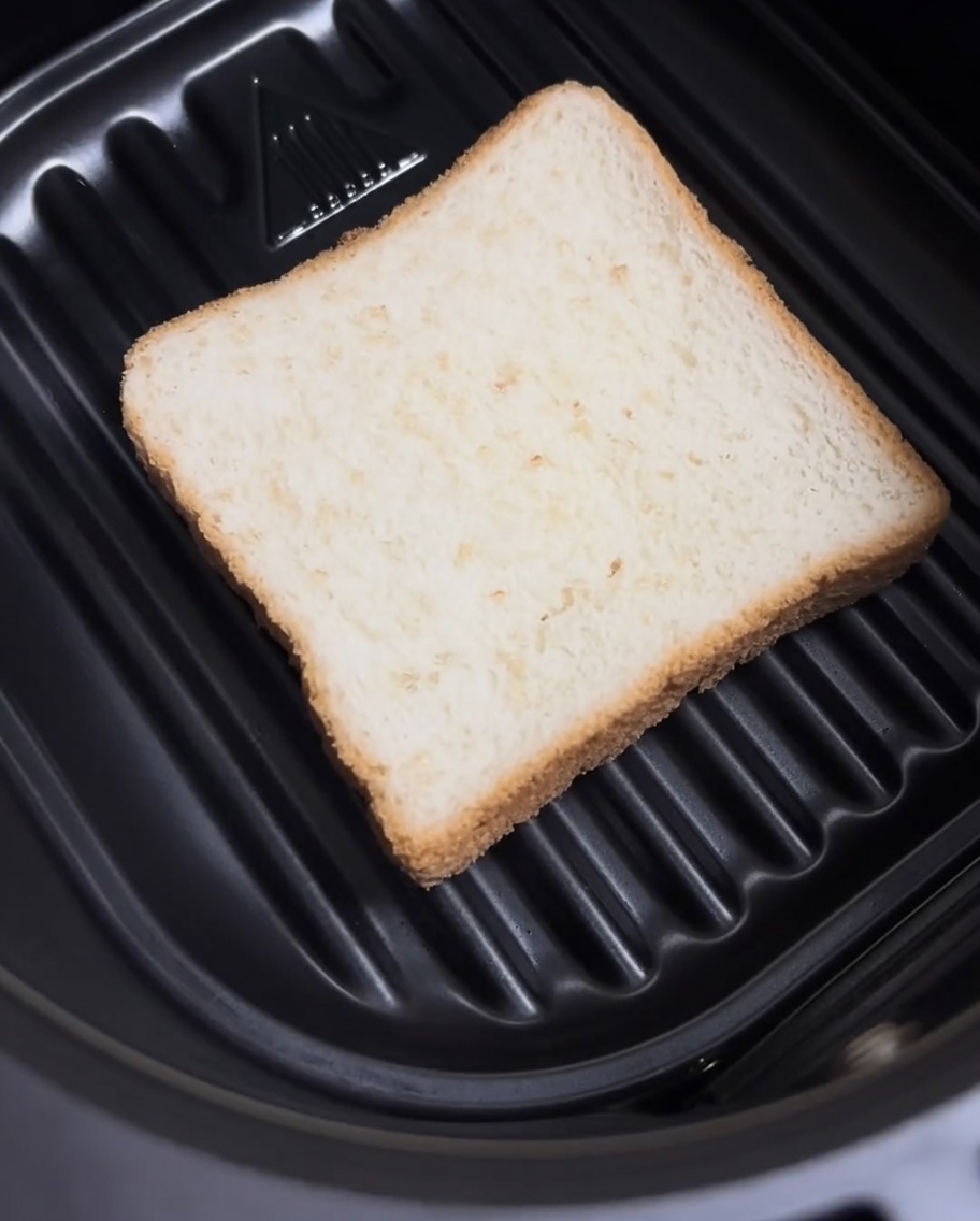 Eine einfache Scheibe Weißbrot, die flach auf dem Boden eines Heißluftfritteusen-Korbs liegt.