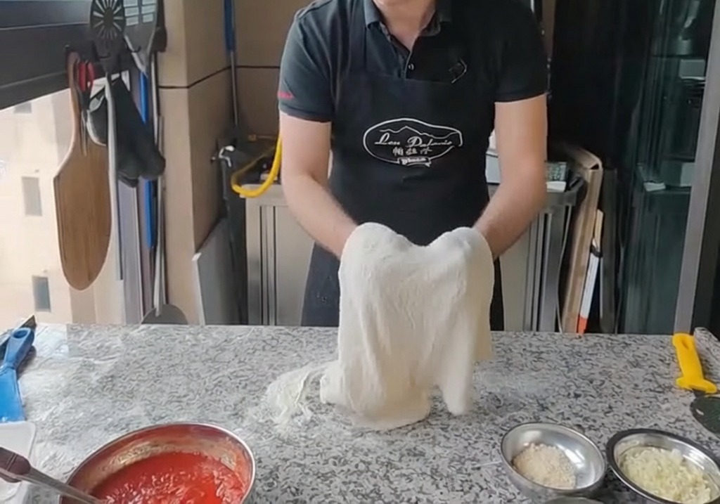 Der Pizzateig wird über die Knöchel beider Hände vertikal gedehnt.
