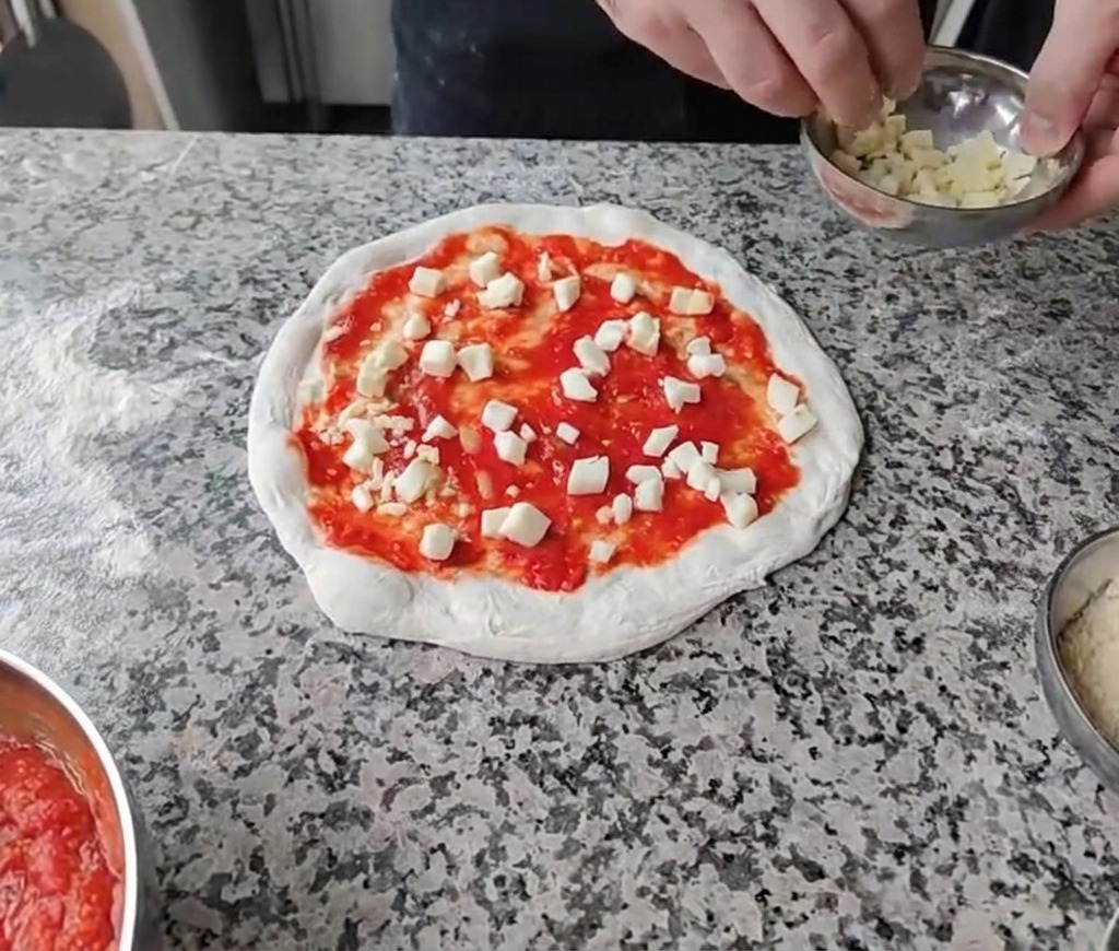 Gewürfelte Käsesorten werden gleichmäßig auf der Tomatensoße verteilt.