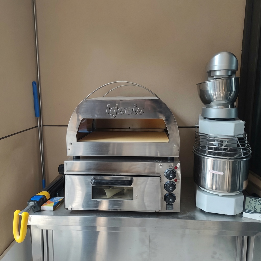 Die rohe Pizza wird mit einem Schieber in den heißen Pizzaofen geschoben.