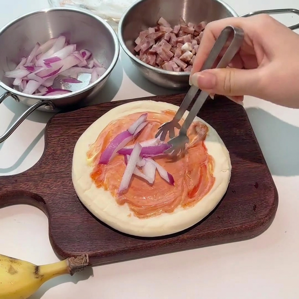 Eine Zange legt frische rote Zwiebelscheiben auf den mit Sauce bestrichenen Pizzaboden.