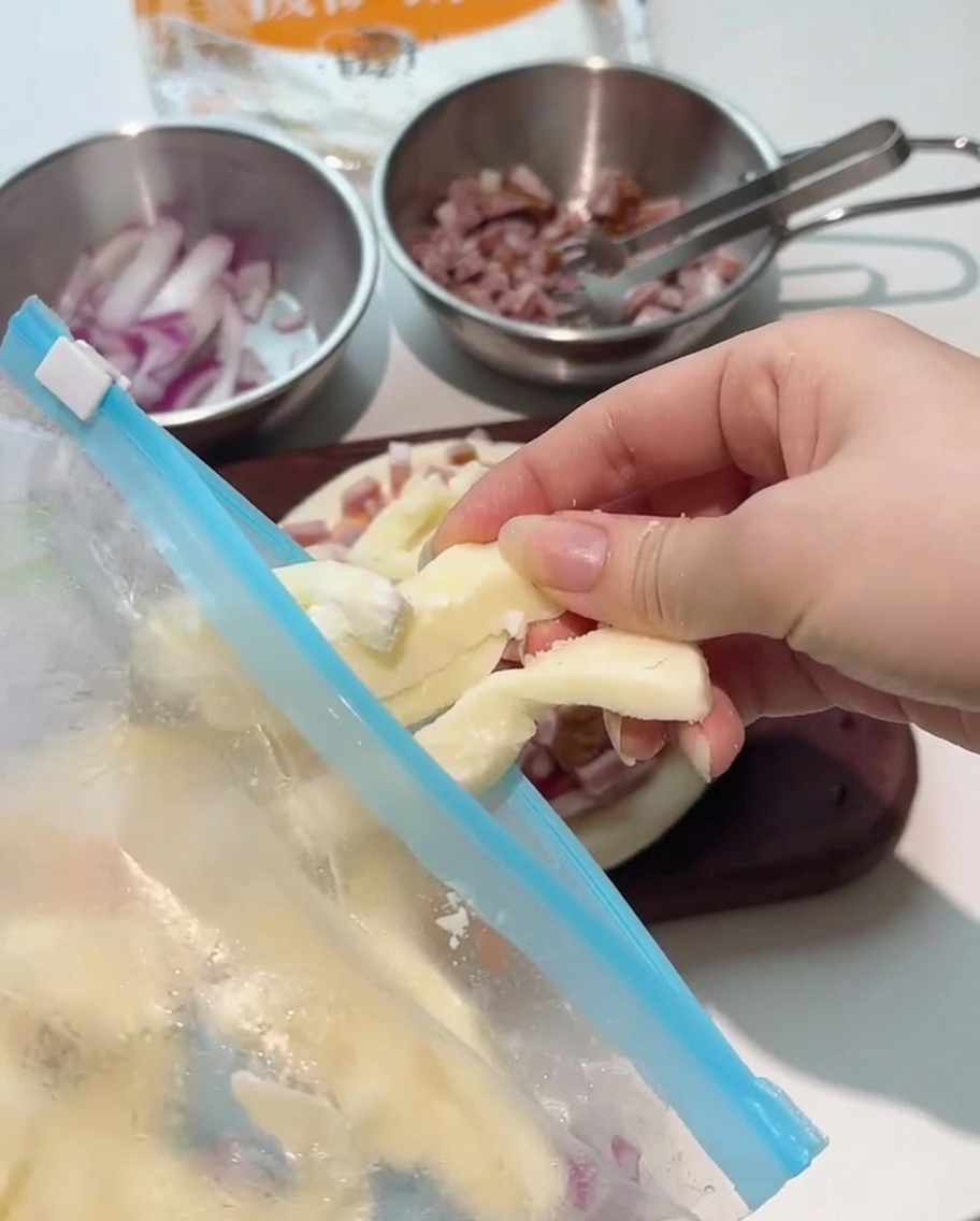 Dicke Mozzarella-Streifen werden über den belegten Pizzaboden gelegt.