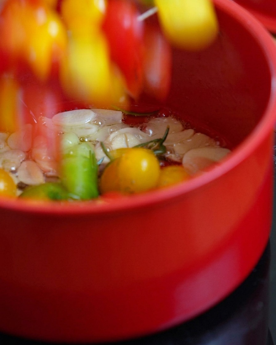 Halbierte Kirschtomaten werden zum aromatisierten Öl in den Topf gegeben.