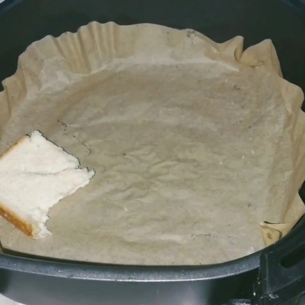 Ein Nahaufnahme von Weißbrotscheiben, die ordentlich auf Backpapier im Airfryer-Korb liegen.