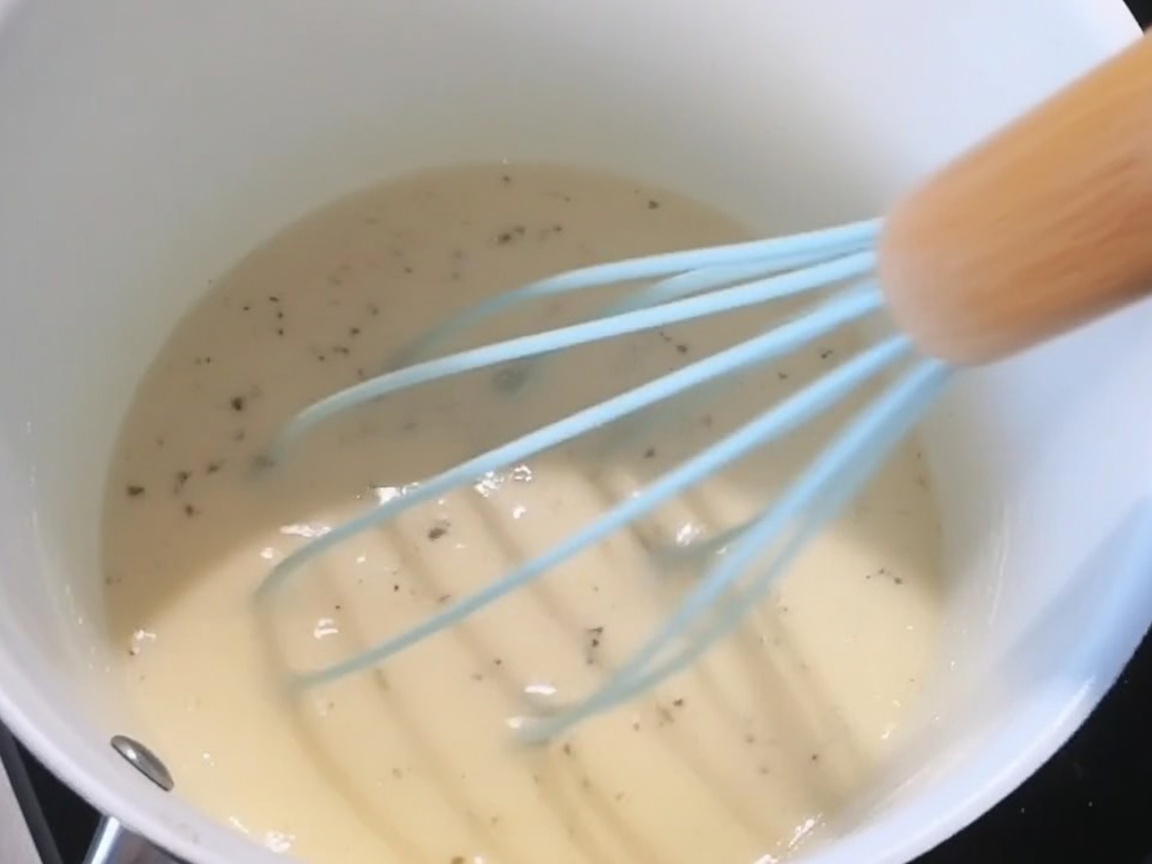 Salz, schwarzer Pfeffer und geriebener Käse werden in die cremige weiße Sauce gegeben.