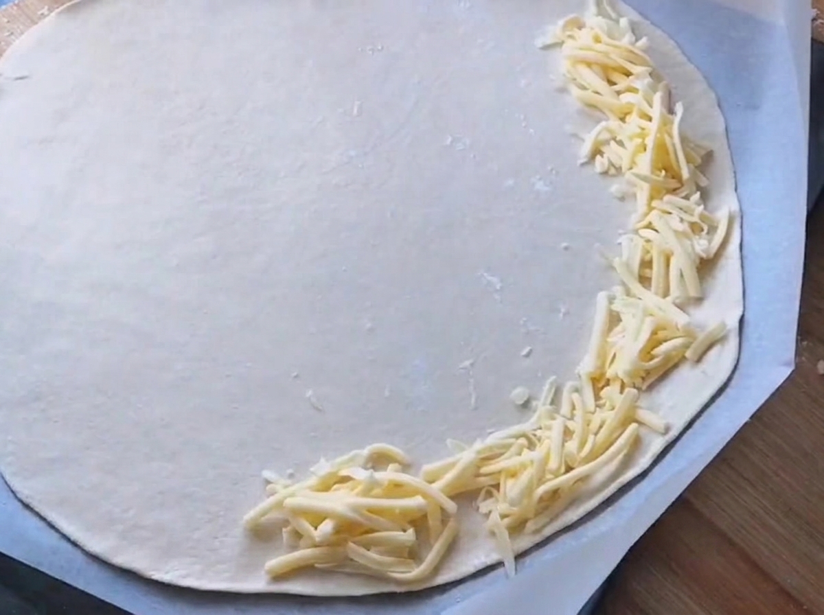Weiße Sauce wird auf einem runden Pizzateig verstrichen.
