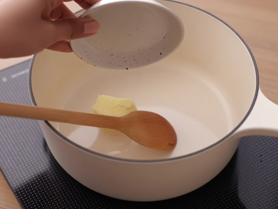 Ein Stück Butter schmilzt in einem kleinen weißen Topf auf dem Herd.