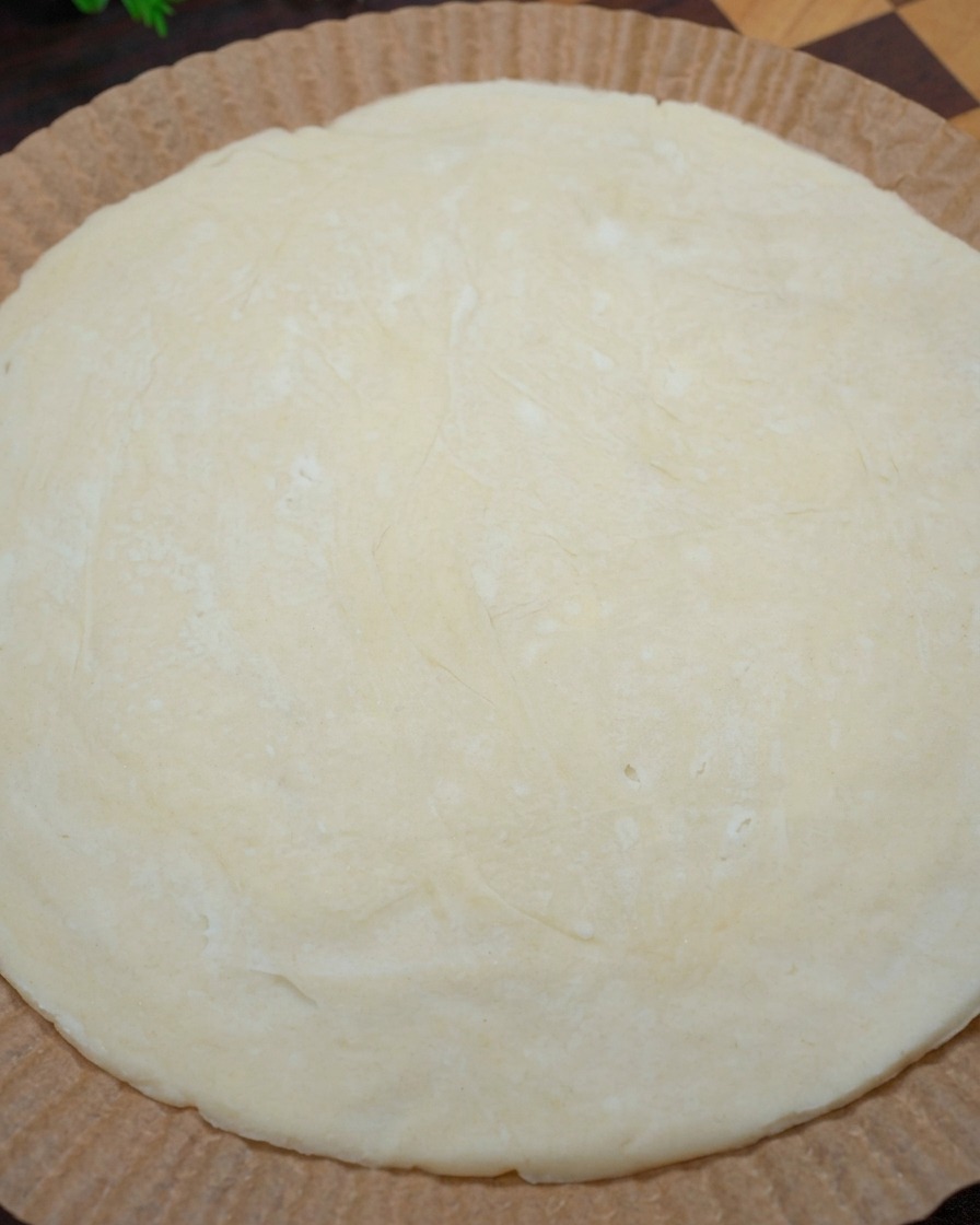 Nahaufnahme von Händen, die die Ränder eines rohen, runden Frühlingszwiebel-Pfannkuchens auf Backpapier zu einem Pizzarand formen.